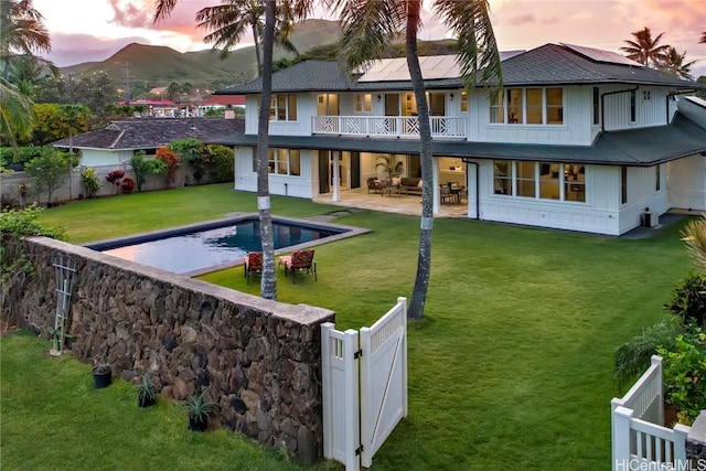 back house at dusk with a lawn, a fenced in pool, solar panels, a balcony, and a patio