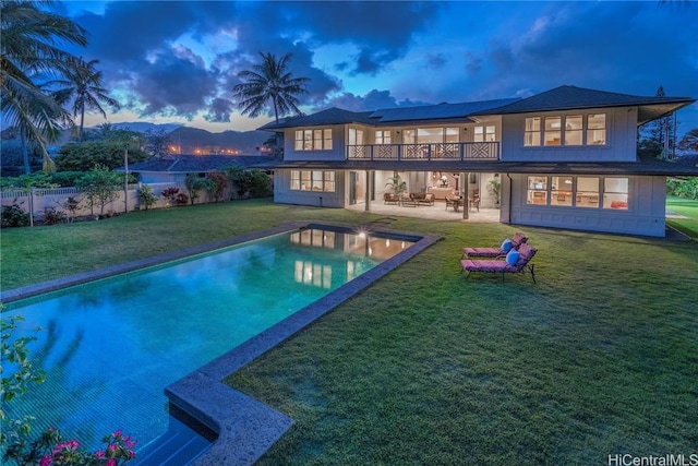 back house at dusk with a fenced in pool, a patio area, and a yard