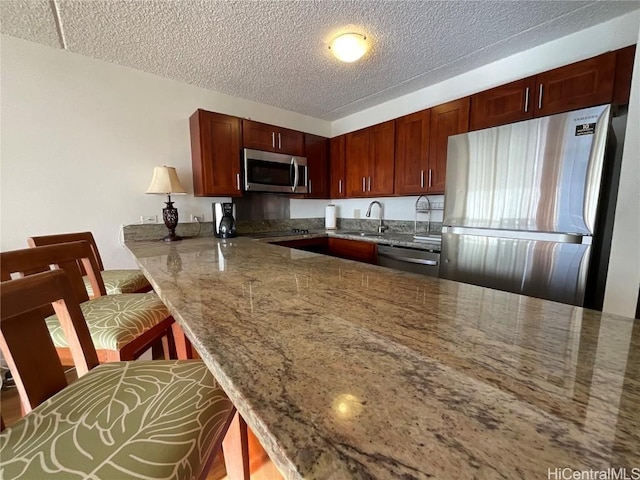 kitchen with kitchen peninsula, a textured ceiling, stone countertops, a kitchen bar, and appliances with stainless steel finishes