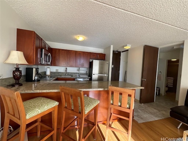 kitchen featuring sink, light hardwood / wood-style flooring, kitchen peninsula, a kitchen bar, and appliances with stainless steel finishes