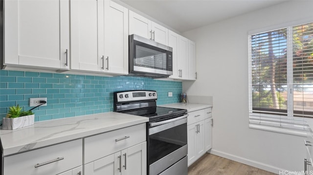 kitchen with backsplash, white cabinets, light wood-type flooring, light stone counters, and stainless steel appliances