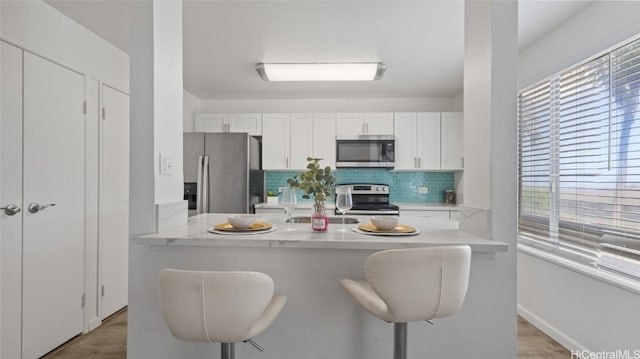 kitchen featuring light stone countertops, appliances with stainless steel finishes, backsplash, a breakfast bar, and white cabinetry