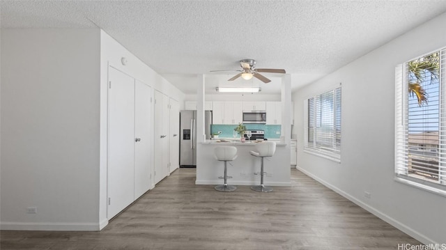 kitchen with a breakfast bar, backsplash, white cabinets, ceiling fan, and stainless steel appliances