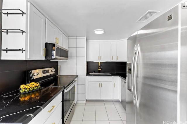 kitchen featuring white cabinets, sink, dark stone countertops, appliances with stainless steel finishes, and light tile patterned flooring