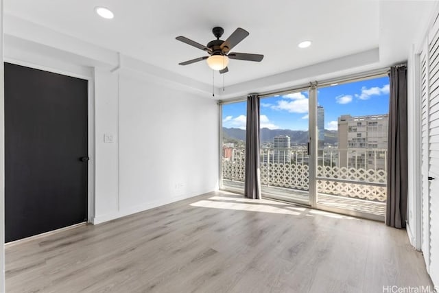 spare room with a tray ceiling, ceiling fan, and light hardwood / wood-style flooring