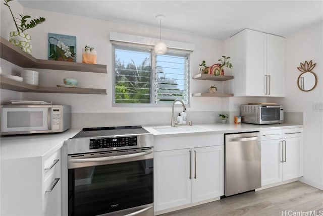 kitchen with stove, stainless steel dishwasher, sink, white cabinetry, and hanging light fixtures