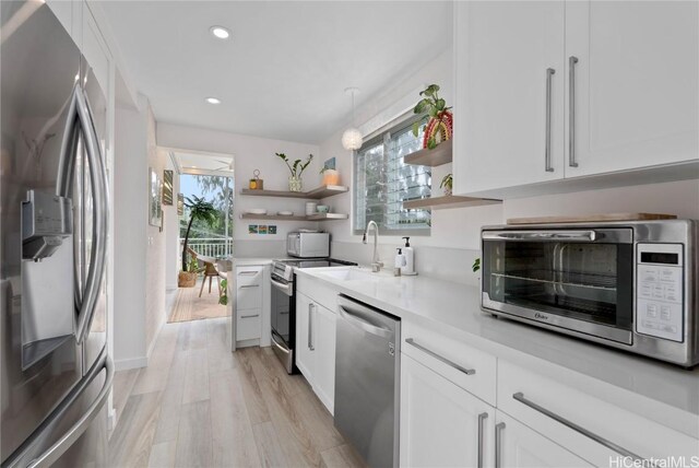 kitchen with sink, hanging light fixtures, stainless steel appliances, light hardwood / wood-style floors, and white cabinets