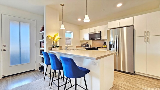 kitchen featuring kitchen peninsula, a breakfast bar area, appliances with stainless steel finishes, hanging light fixtures, and white cabinets