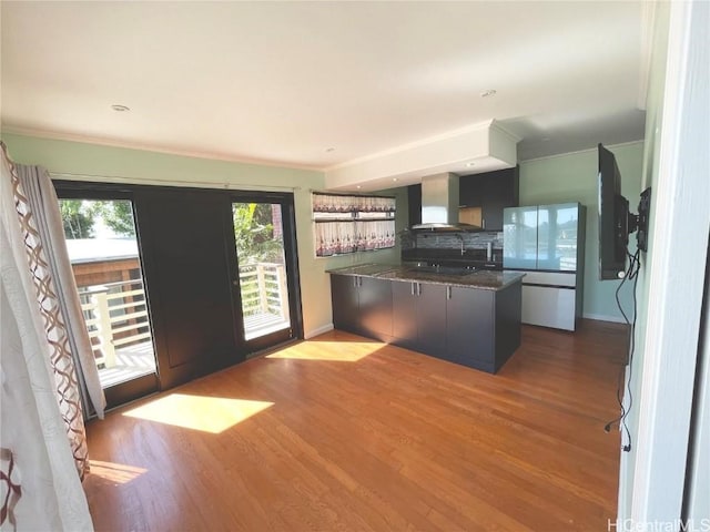 kitchen with kitchen peninsula, light hardwood / wood-style floors, wall chimney range hood, and ornamental molding