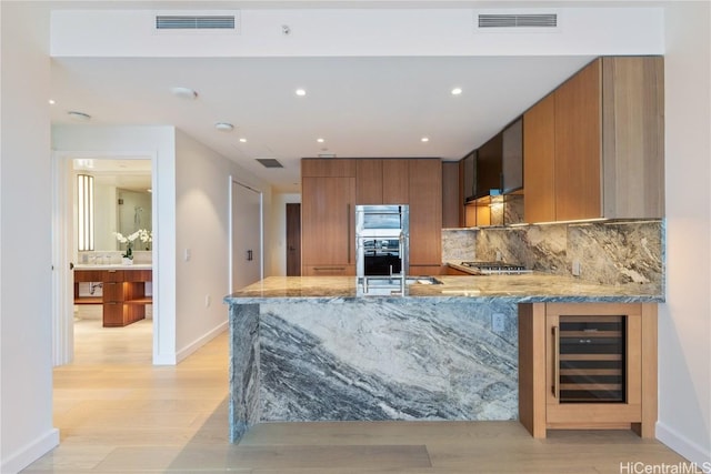 kitchen with kitchen peninsula, tasteful backsplash, stainless steel gas cooktop, sink, and wine cooler