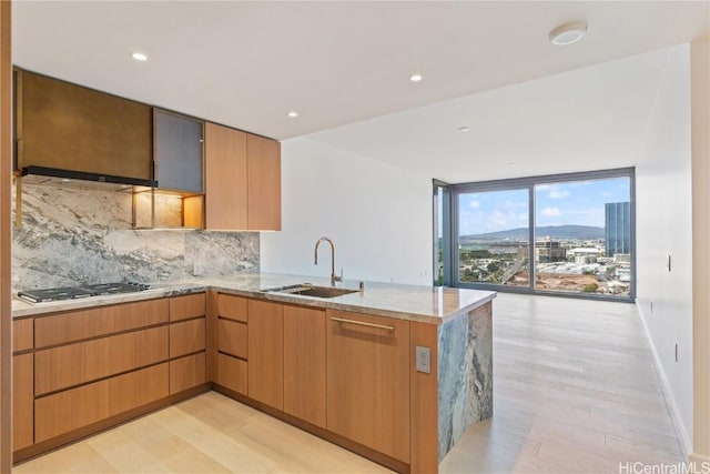 kitchen featuring kitchen peninsula, expansive windows, stainless steel gas cooktop, sink, and light hardwood / wood-style flooring