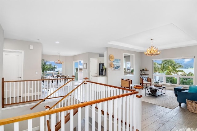 corridor featuring a raised ceiling, an upstairs landing, light wood-type flooring, a chandelier, and recessed lighting