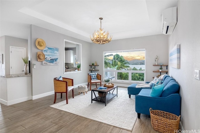 living room with an inviting chandelier, a wall mounted air conditioner, a tray ceiling, and hardwood / wood-style floors