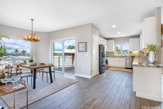 kitchen featuring appliances with stainless steel finishes, pendant lighting, white cabinets, a chandelier, and plenty of natural light