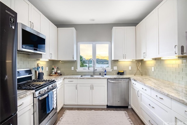 kitchen featuring sink, stainless steel appliances, light stone countertops, decorative backsplash, and white cabinets