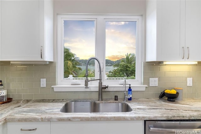 kitchen with a wealth of natural light, dishwasher, sink, white cabinets, and light stone countertops