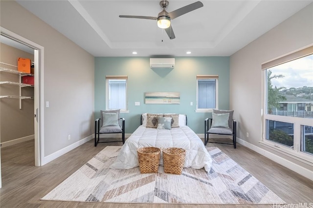 bedroom with a walk in closet, an AC wall unit, a raised ceiling, a closet, and ceiling fan