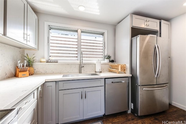 kitchen featuring appliances with stainless steel finishes, backsplash, dark wood-type flooring, light stone countertops, and sink