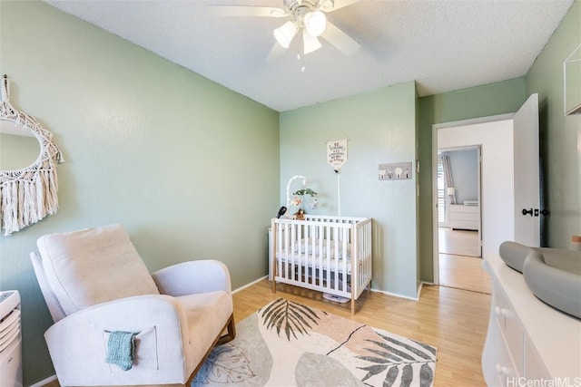 bedroom with ceiling fan, a textured ceiling, a nursery area, and light wood-type flooring