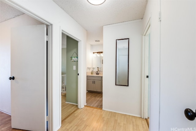 corridor with light wood-type flooring, sink, and a textured ceiling