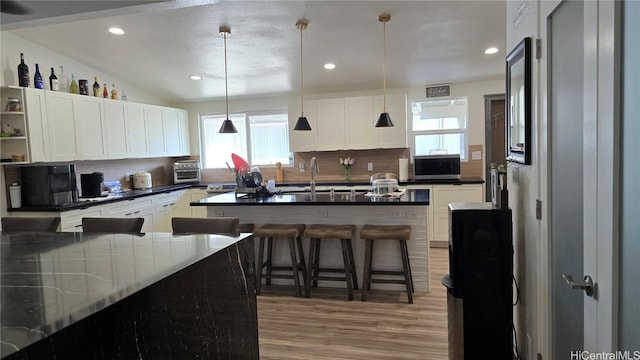 kitchen with a kitchen bar, decorative light fixtures, white cabinetry, and tasteful backsplash