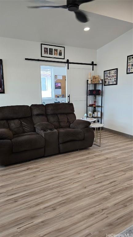 living room featuring ceiling fan, a barn door, and light wood-type flooring