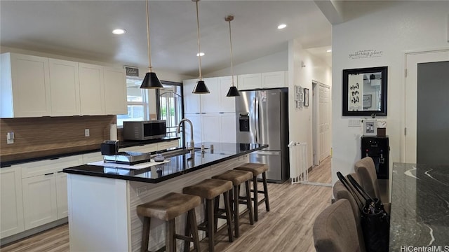 kitchen featuring white cabinets, appliances with stainless steel finishes, decorative light fixtures, vaulted ceiling, and a center island with sink