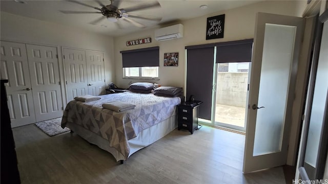 bedroom with an AC wall unit, light wood-type flooring, ceiling fan, and multiple closets