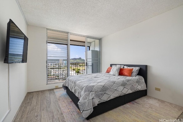 bedroom featuring access to outside, expansive windows, wood-type flooring, and a textured ceiling