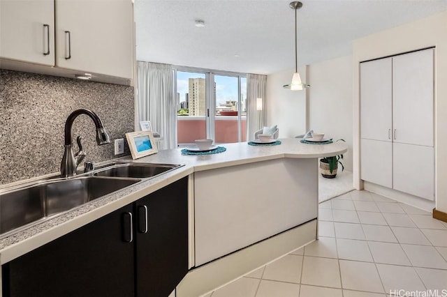 kitchen featuring decorative backsplash, sink, pendant lighting, light tile patterned floors, and white cabinets