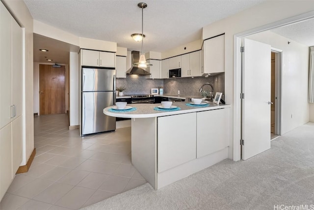 kitchen featuring white cabinetry, pendant lighting, wall chimney range hood, and appliances with stainless steel finishes