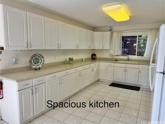 kitchen with light tile patterned floors, white refrigerator, white cabinetry, and sink