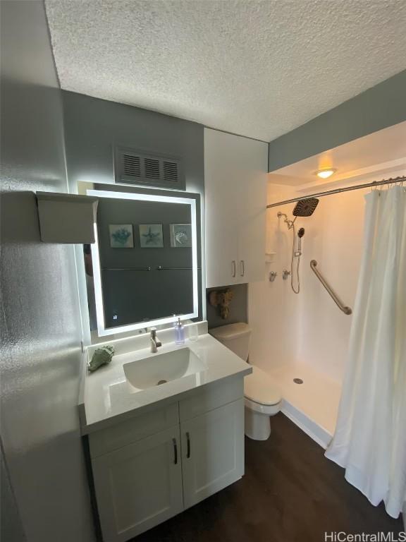 bathroom featuring walk in shower, wood-type flooring, a textured ceiling, toilet, and vanity