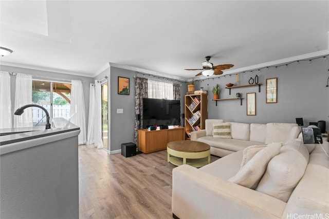 living room featuring crown molding, light wood-type flooring, sink, and ceiling fan