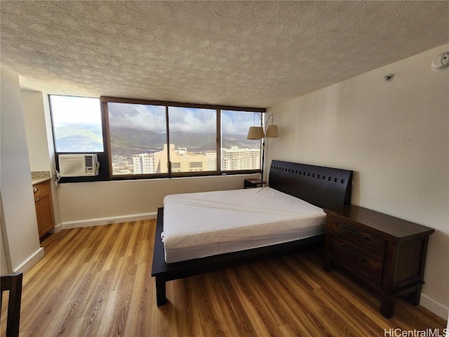 bedroom with a textured ceiling, light hardwood / wood-style flooring, and cooling unit