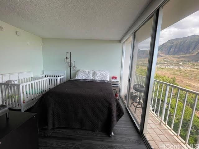 bedroom featuring access to outside, a mountain view, hardwood / wood-style floors, and a textured ceiling