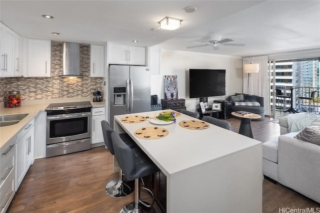 kitchen with appliances with stainless steel finishes, backsplash, wall chimney range hood, white cabinets, and a center island