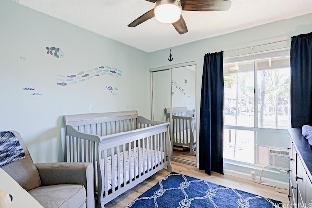 bedroom featuring a ceiling fan, wood finished floors, a wall mounted air conditioner, a nursery area, and a closet