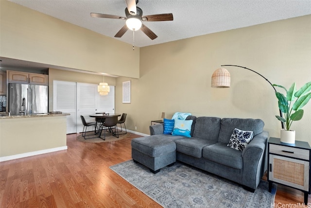 living room featuring lofted ceiling, ceiling fan, wood-type flooring, and a textured ceiling