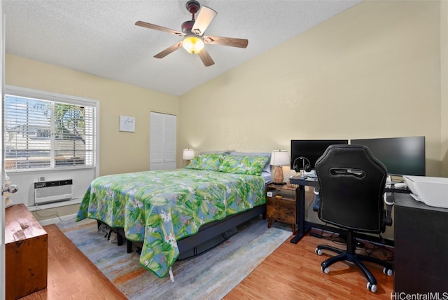 bedroom with hardwood / wood-style floors, lofted ceiling, ceiling fan, a wall unit AC, and a closet