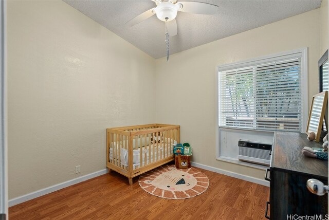 bedroom featuring vaulted ceiling, a wall mounted AC, ceiling fan, a crib, and light hardwood / wood-style floors