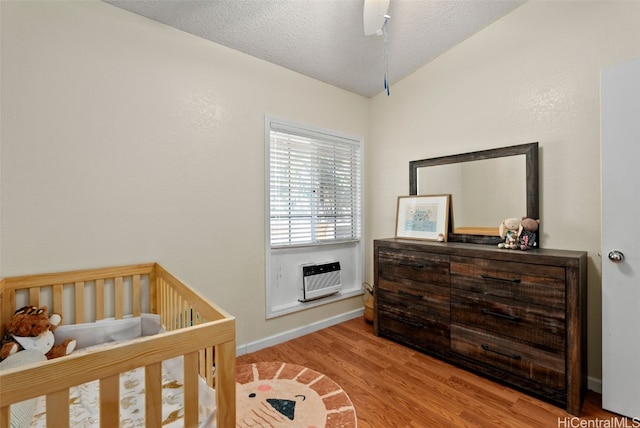 bedroom featuring vaulted ceiling, a textured ceiling, wood finished floors, a wall mounted air conditioner, and baseboards