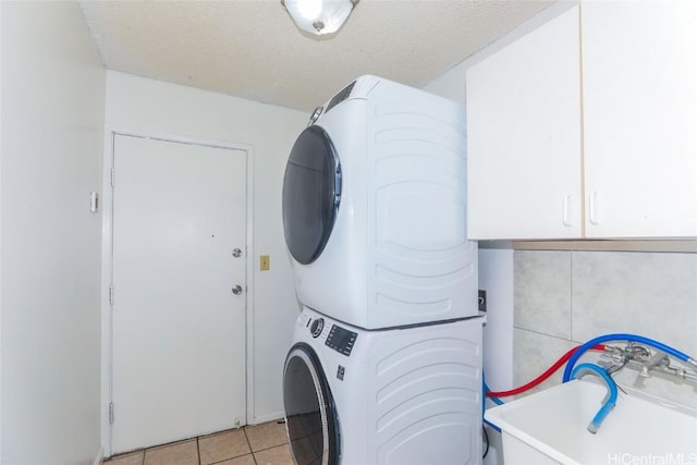 laundry room featuring cabinets, stacked washing maching and dryer, a textured ceiling, light tile patterned floors, and tile walls