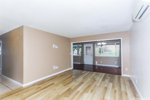 spare room with a chandelier, light hardwood / wood-style floors, and a wall mounted AC