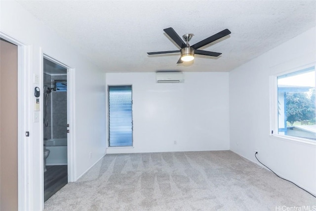 spare room featuring ceiling fan, light colored carpet, an AC wall unit, and a textured ceiling