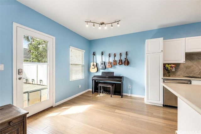 kitchen featuring baseboards, light wood finished floors, white cabinets, dishwasher, and tasteful backsplash