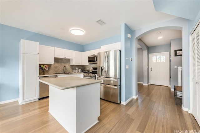 kitchen featuring arched walkways, visible vents, white cabinetry, appliances with stainless steel finishes, and light wood-type flooring