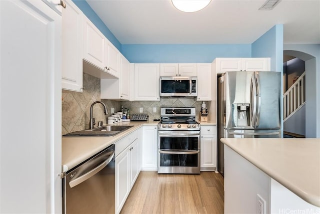 kitchen featuring stainless steel appliances, a sink, white cabinets, light countertops, and decorative backsplash