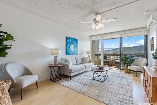 living area featuring a wall mounted AC, a ceiling fan, a textured ceiling, light wood-type flooring, and baseboards