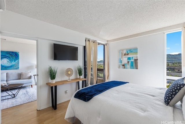 bedroom with multiple windows, a textured ceiling, baseboards, and wood finished floors